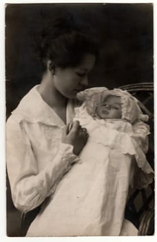 GERMANY - APRIL 25, 1918: Vintage photo shows woman with baby -newborn in swaddling clothes. Retro black and white studio photography.