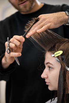 Professional male hairdresser with scissors cutting female hair in salon
