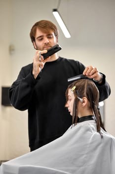 Professional male hairdresser with scissors cutting female hair in salon