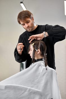 Professional male hairdresser with scissors cutting female hair in salon