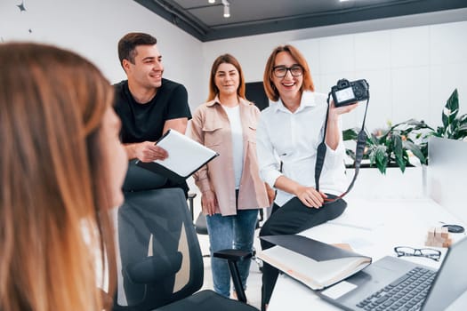 Group of business people in formal clothes indoors in the office looking at photos on the camera.