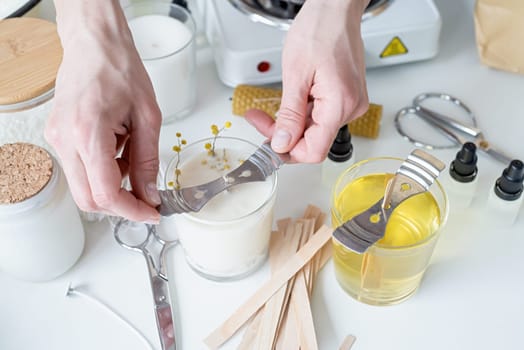 Creative hobby of candle making at home. Woman making decorative aroma candle at table, setting wooden wick into glass with melted soy wax