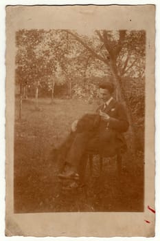 MALENICE NAD VOLYNKOU, THE CZECHOSLOVAK REPUBLIC - AUGUST 28, 1924: Vintage photo shows man sits on a chair in the garden. Retro black and white photography with sepia effect.