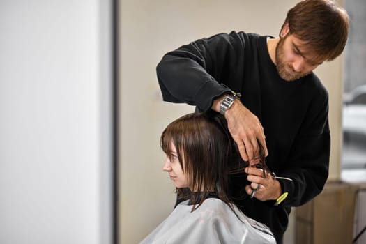 Professional male hairdresser with scissors cutting female hair in salon