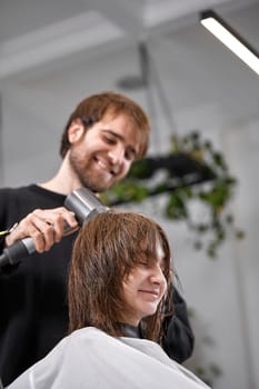 man hairdresser dries female hair with hairdryer after washing in the beauty salon.