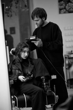 man hairdresser using hair dryer for female hair after washing in the beauty salon.