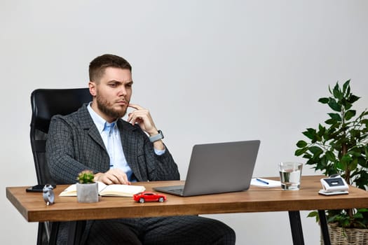 young man sitting on chair at table and resting, using laptop on white wall background