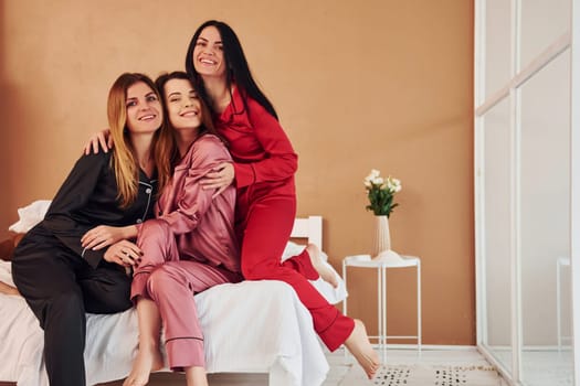 Cheerful young women in pajamas sitting indoors at daytime together.