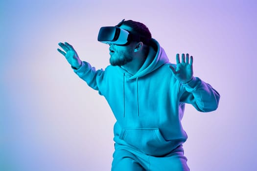 man in sweatshirt using virtual reality glasses and playing video games on blue background. Neon lighting