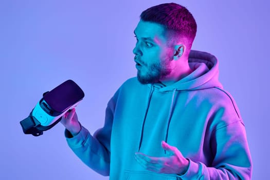 man in sweatshirt using virtual reality glasses and playing video games on blue background. Neon lighting