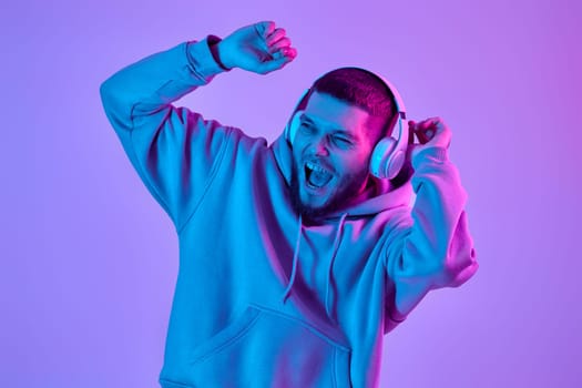 handsome man listening to music with wireless headphones on purple neon background. Neon lighting