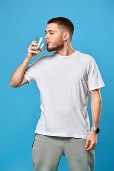 handsome bearded man drinks water from a glass on blue background