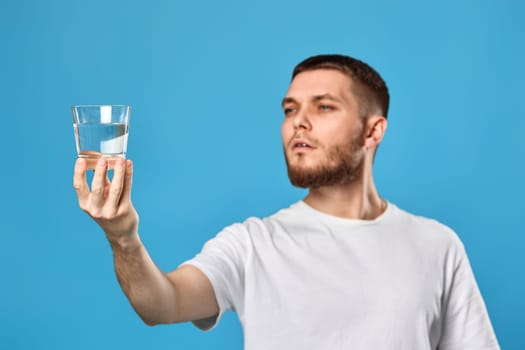 handsome bearded man with drinking glass of water smiling happy on blue background. focus on glass