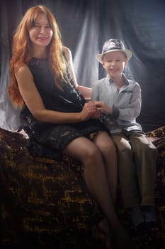 Woman with boy in hat. Mom with son on a dark background. Family portrait with mother with red hair and boy having fun together