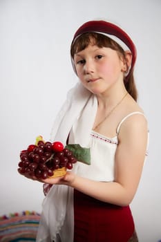 Portrait of Little girl in a stylized Tatar national costume with berries and a brush of grapes on a white background in the studio. Photo shoot of funny young teenager who is not a professional model