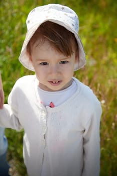 Portrait of little girl with Asian eyes in a meadow or field with grass and flowers on a sunny summer day