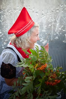 A Girl in black school uniform, white apron and red tie near fountain water with bouquet of flowers. Nostalgia photo shoot of teenager of female pioneer from USSR costume for September 1 or graduation