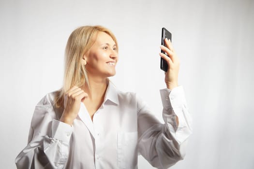 Portrait of a smiling casual woman holding smartphone over white background. The girl is chatting and taking selfies. Business lady with cell phone. Copy space