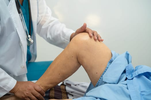 Asian doctor physiotherapist examining, massaging and treatment knee and leg of senior patient in orthopedist medical clinic nurse hospital.