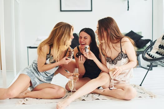 Cheerful young women in pajamas sitting on the floor indoors at daytime together.