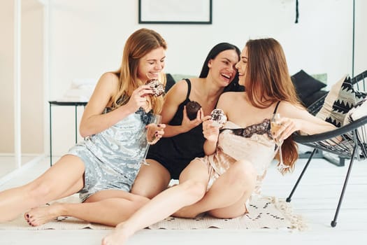 Cheerful young women in pajamas sitting on the floor indoors at daytime together.