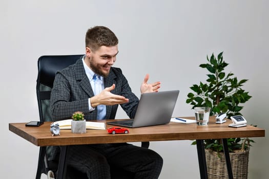 young friendly man talking at laptop webcam, sitting on chair at desk, using laptop pc computer