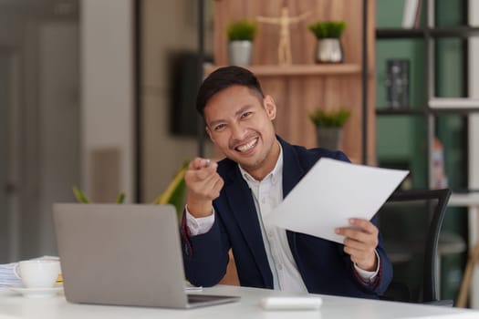 Smiling Asian Banker makes financial report and studies annual figures, analyzes profits. Accountant checks status of financial.