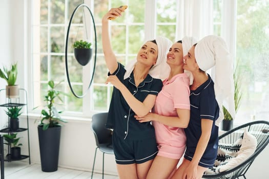 Cheerful young women in pajamas having fun indoors at daytime together.