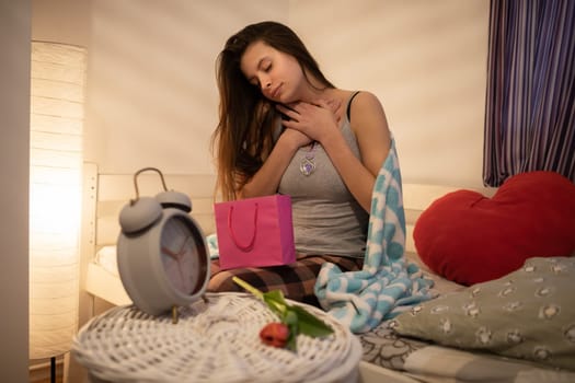 A woman received jewelry as a gift for Valentine's Day. A large alarm clock stands on the bedside table.