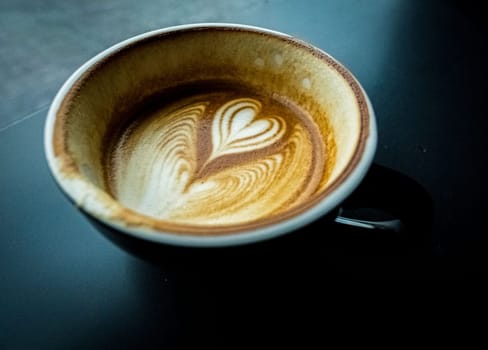 cup of hot latte coffee with love heart shape foam milk over dark background
