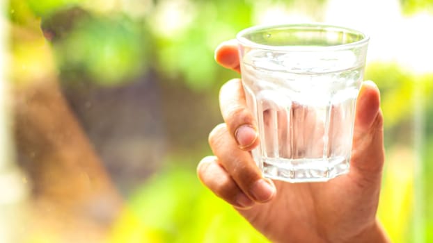 hand holds clear water in glass . hand holding A clear glass of clean mineral water . Concept of environment protection, healthy drink. nature blurred background