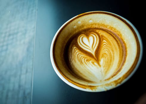 cup of hot latte coffee with love heart shape foam milk over dark background