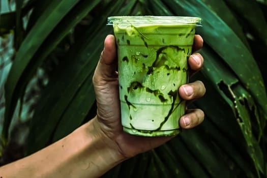 iced Green matcha tea mixed with ice cube and milk in latte glass  with green nature background