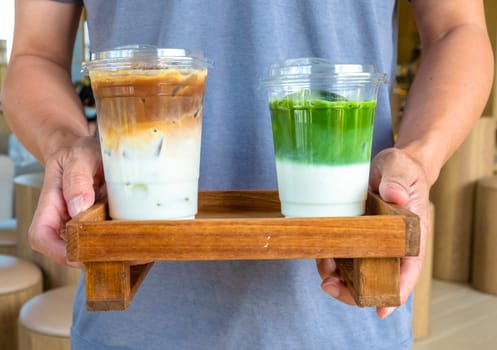 A man is holding a ice latte coffee and matcha latte on wooden plate