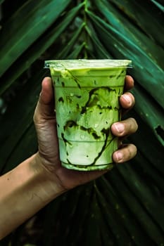 iced Green matcha tea mixed with ice cube and milk in latte glass  with green nature background