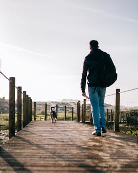 Low angle view of man with backpack on morning walk with his dog through a wooden path.