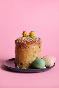 Still life with Easter cake and colorful eggs on navy ceramic plate, isolated over pink background. Vertical studio shot. The symbol of the resurrection of Jesus Christ. Orthodox and catholic holiday