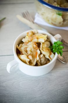 cooked dumplings with potatoes and fried onions, in a bowl on a wooden table.