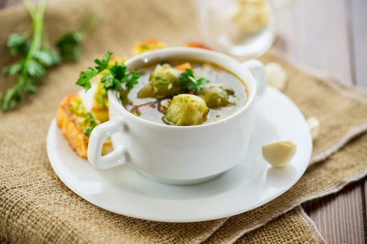 Hot cooked soup with Brussels sprouts, vegetables and croutons, in a plate on a wooden table.
