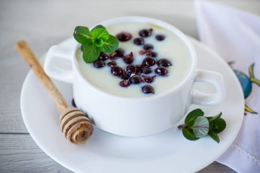 Cooked milk semolina porridge with berries and honey in a plate, on a wooden table.