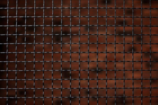 Black metal grating on natural brick background, steel fence indoors close up. Wallpaper metallic wire barrier. Stylized design solution in the interior. Security and safety concept.