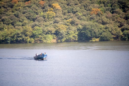 aerial drone shot of handmade boat used by rural villagers to cross over lakes like Dhebar, Pichola from tree covered mountains as a ferry service