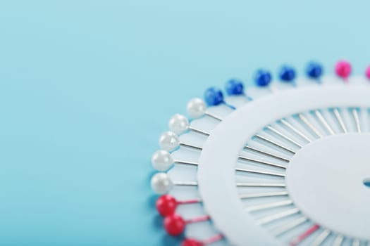 A set of multicolored needles pins in a round platform on a blue background with free space