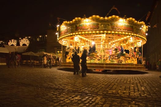 London, United Kingdom - November 25th, 2006: People walking around and watching carousel illuminated in evening at Covent Garden which is popular tourist spot in UK capital.
