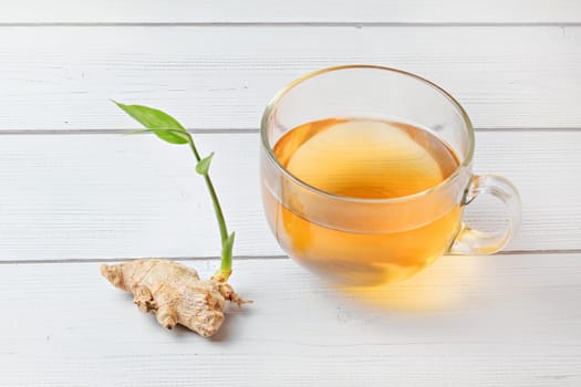 Cup of freshly brewed amber tea, hot steam makes tiny wet drops on glass. Dry ginger root with green sprout next to it.