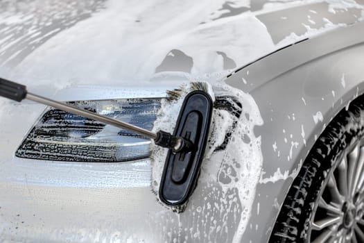 Detail on silver car headlight washed in manual carwash, brush cleaning the glass.