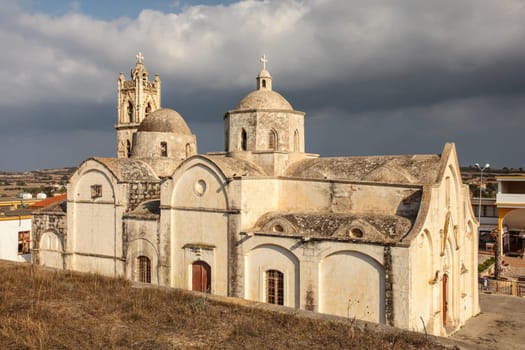 Ayios Synesios Church in Rizokarpaso (Dipkarpaz), lit by afternoon sun, some heavy clouds in background. This northern Cyprus town is known for Christians and Muslims living in harmony.