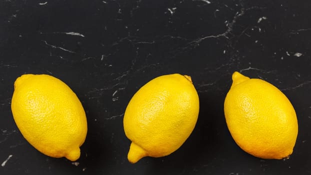 Tabletop view, three whole ripe lemons on black stone board. Space for text above