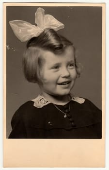 THE CZECHOSLOVAK REPUBLIC - CIRCA 1950s: Vintage photo shows a portrait of a small cute girl with ribbon in hair. Retro black and white photography. Circa 1950s.