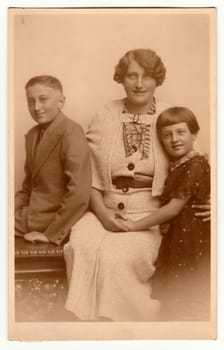 THE CZECHOSLOVAK REPUBLIC - CIRCA 1920s: Vintage photo shows family - mother, son and daughter. Retro black and white studio photography with sepia effect. Circa 1940s.